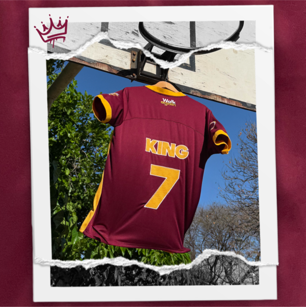 Jersey bordó combinado con amber, holgado y fresco confeccionado en polyester. Diseño exclusivo con múltiples bordados. Frente: Imagen de Jesús venciendo al diablo en una jugada de básquet + texto KING. Espalda: texto KING y el número 7. Manga derecha: escudo con pelota básquet y la frase “He is the King”. Manga izquierda: texto “You’ll never walk alone again“.