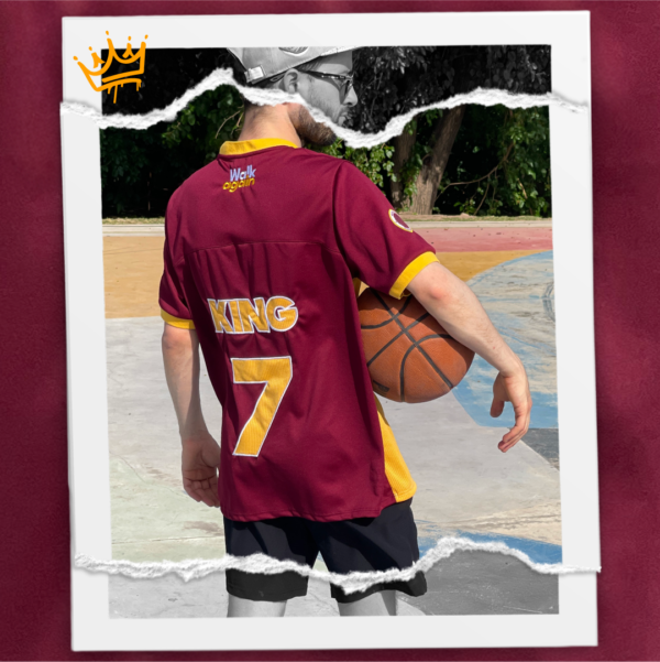 Jersey bordó combinado con amber, holgado y fresco confeccionado en polyester. Diseño exclusivo con múltiples bordados. Frente: Imagen de Jesús venciendo al diablo en una jugada de básquet + texto KING. Espalda: texto KING y el número 7. Manga derecha: escudo con pelota básquet y la frase “He is the King”. Manga izquierda: texto “You’ll never walk alone again“.